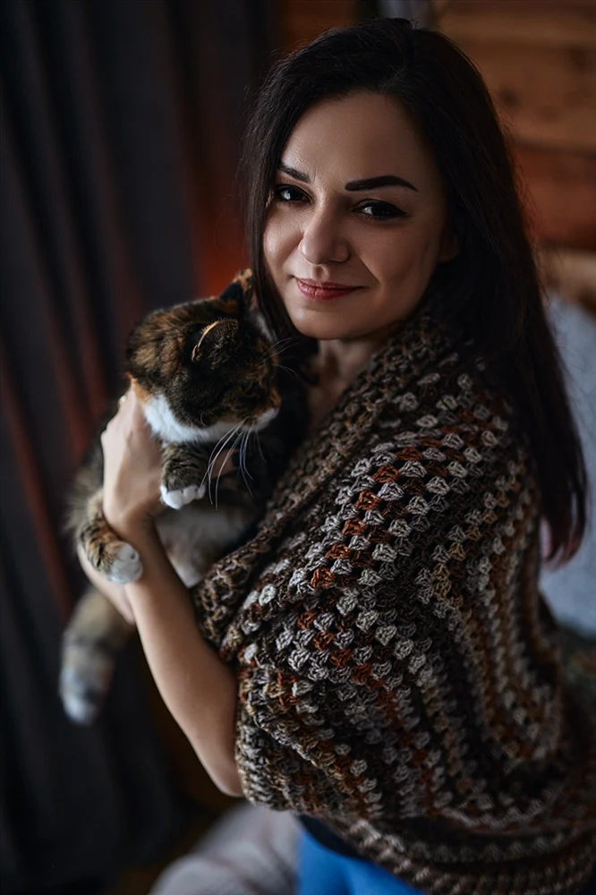 Sylwia Karolina Janiec, Polish language teacher, smiling and holding a calico cat in a cosy wooden interior
